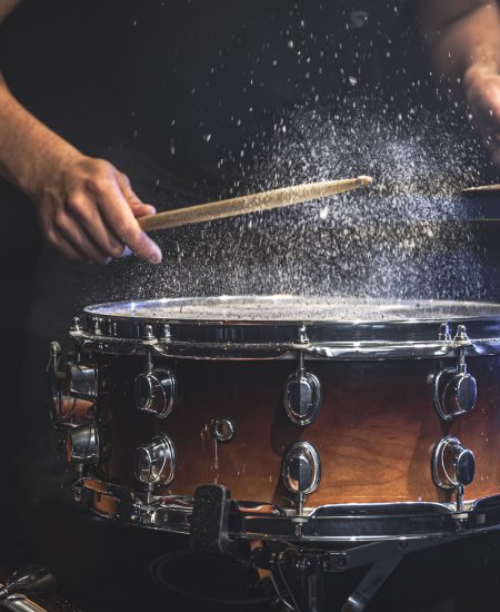 A male drummer plays snare drum with drumsticks in a dark room.